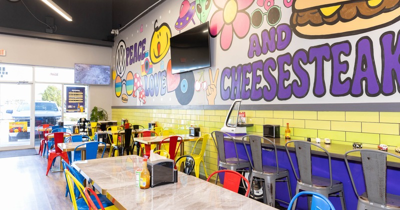Interior of a diner with colorful chairs, a vibrant mural and overhead fluorescent lights.