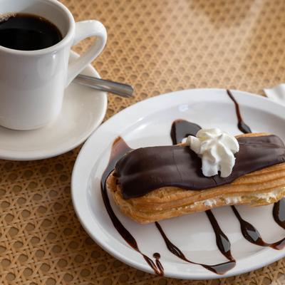 Chocolate eclair beside a cup of black coffee.