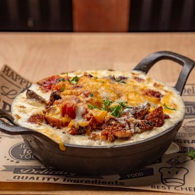 Loaded mac and cheese served in a small, black cast-iron skillet with two handles.