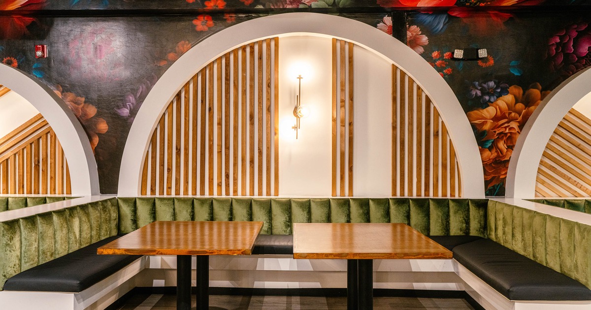 Booth - green velvet cushions, two wooden tables, a floral mural backdrop with wooden arches