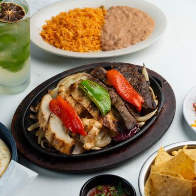 Chicken and steak fajitas served with rice, refried beans, chips, and a mojito.
