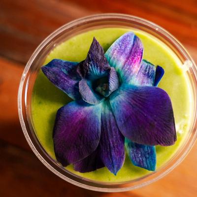 Green smoothie topped with purple flower, top view.