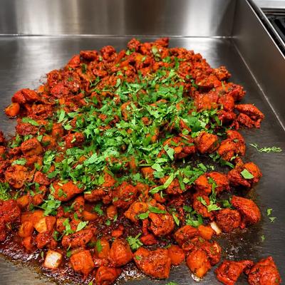 Chicken Tikka tossed on a flat griddle  and garnished with chopped coriander.