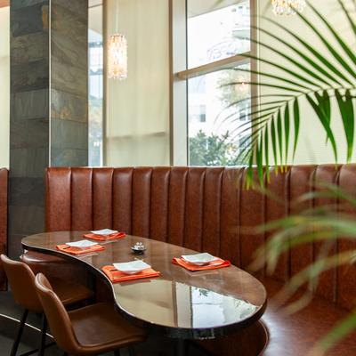 Brown leather booth by the window with an elegant curved table, surrounded by plants.