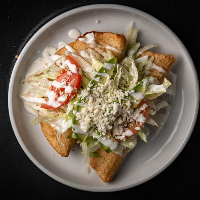 A plate of two empanadas topped with lettuce, tomato, avocado, cheese, and crema.
