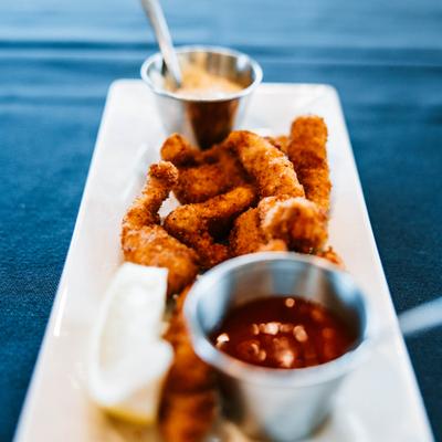 Walleye fingers served with dipping sauces and a lemon wedge.
