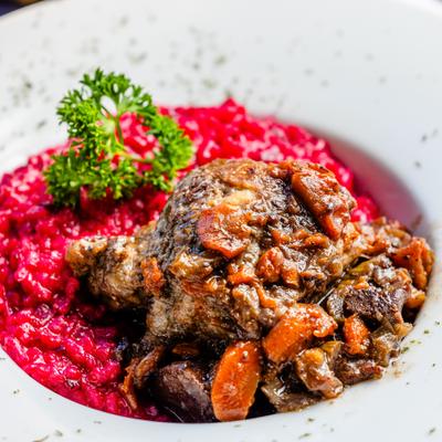 Braised meat served over bright beet risotto, garnished with herbs.