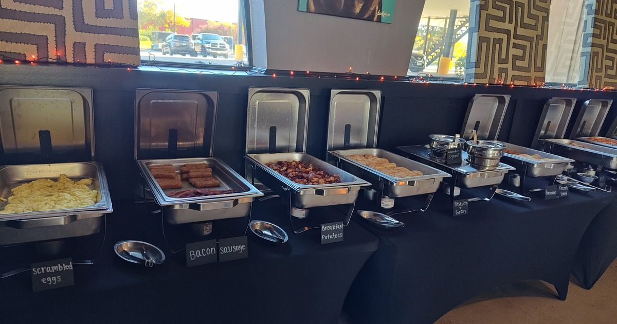 buffet setup with several stainless steel chafing dishes arranged in a row on a black tablecloth