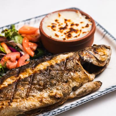 Whole grilled fish served with a baked creamy dish and a salad.