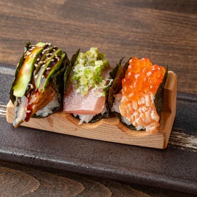 Three sushi hand rolls with avocado, tuna, salmon roe, sesame seeds, and scallions.