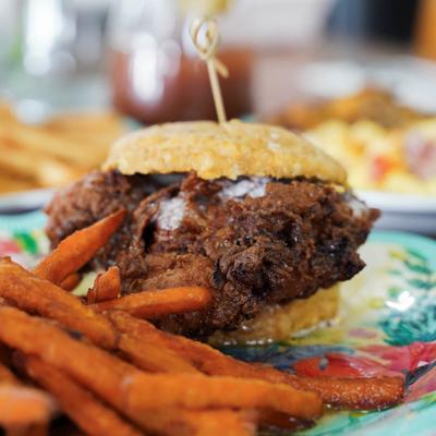A close-up of a Sweet Heat Fried Chicken Biscuit sandwich with sweet potato fries.