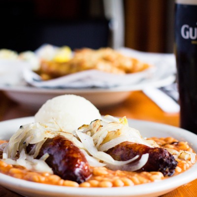 Banger sausages topped with grilled onions on top of baked beans and next to mashed potatoes