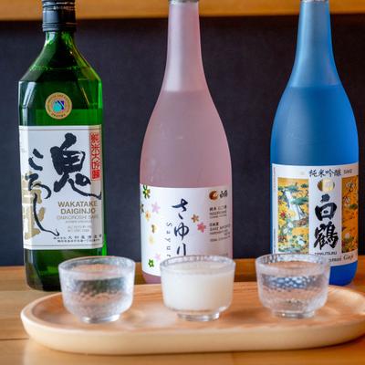 Three different sake bottles with tasting glasses on a wooden tray.