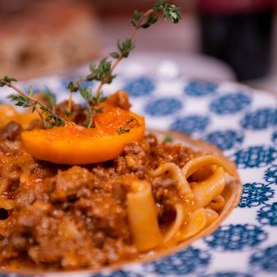 Pappardelle with duck ragu, garnished with a slice of peach and fresh thyme.