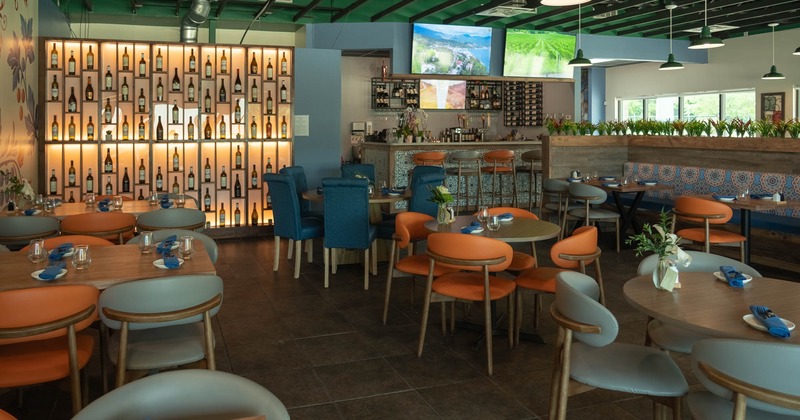 Interior, dining area, wooden top tables for four, tall wine shelf and bar with stools in the back