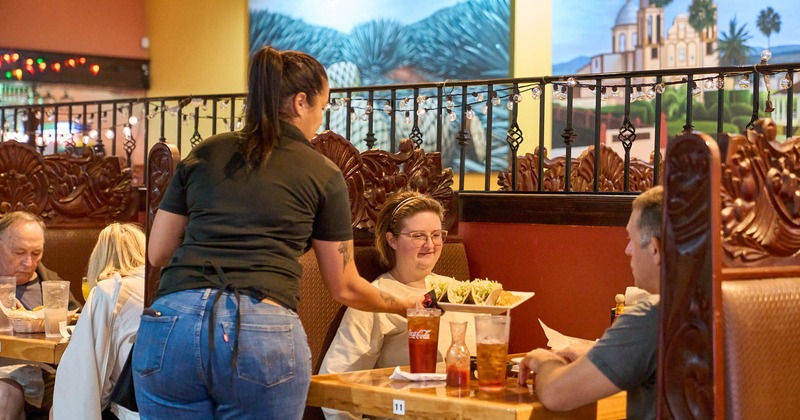 A server serves food to a couple of guests sitting in a booth