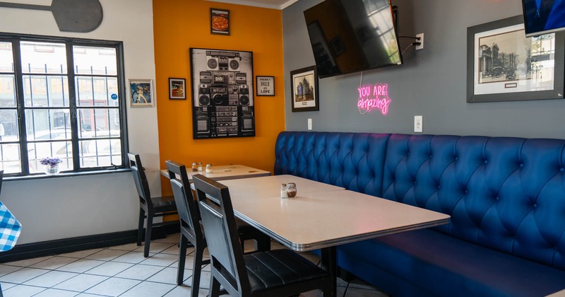 Indoor dining area with blue bench seating, wall decorations, framed artwork, and neon signs