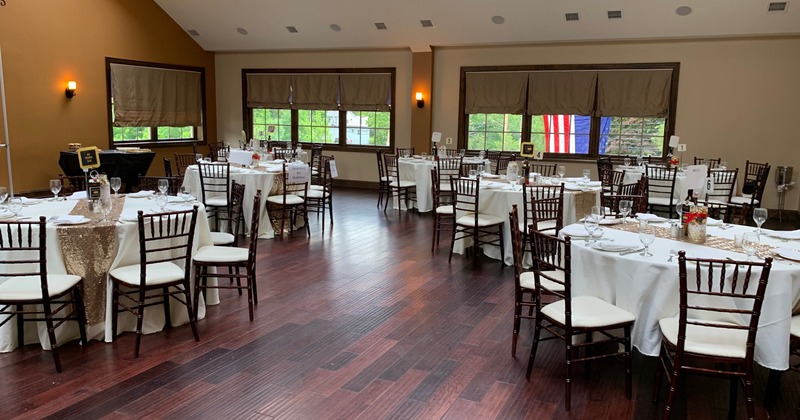Interior, tables and chairs set for an event, white tablecloths, large windows, and a chandelier