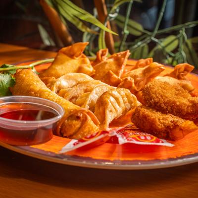 Fried appetizer platter with egg rolls, dumplings, breaded shrimp, and dipping sauce.