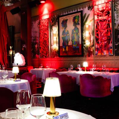 Dining room with set tables, red curtains and framed artwork.