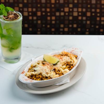 Bowl of seasoned Mexican street corn with melted cheese and lime served with a mojito.