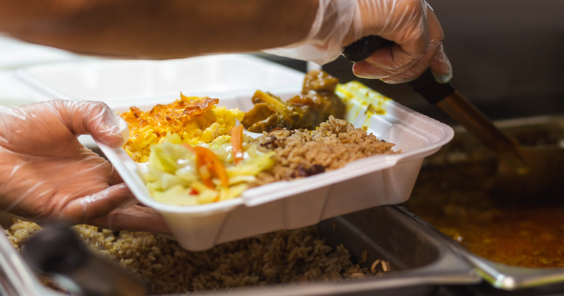 Kitchen staff member placing food into a takeout box, closeup