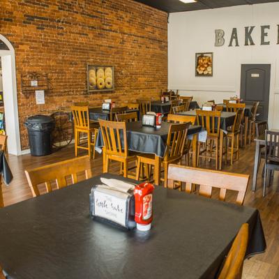 Interior with exposed brick walls, wooden tables and chairs, and a sign on the white wall.