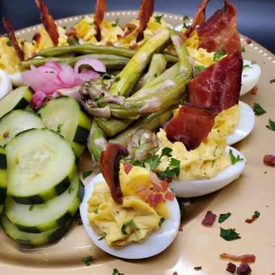 A platter with deviled eggs  alongside slices of cucumber, pickled onion, and asparagus.