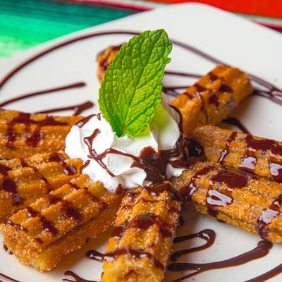Churros plate with whipped cream, chocolate drizzle, and mint garnish.