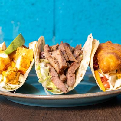 Trio of tacos featuring different fillings served on a rustic blue plate.