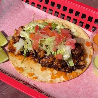 Taco with variety of topings, served on a tray with two dips.