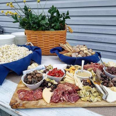 Charcuterie board with meats, cheeses, and dips, beside a basket of popcorn.