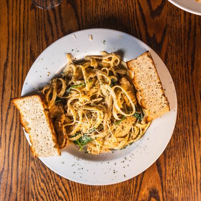 A white plate holds Chicken spinach alfredo with house focaccia, set on a wooden table.