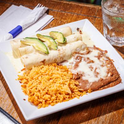 Three chicken enchiladas topped with cheese dip and avocado, served with rice and beans.