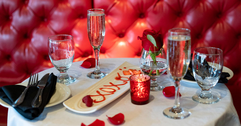 Interior, closeup of a set table with tableware, glasses, red rose and a candle