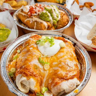 Enchilada style burrito served in a foil container with other dishes in the background.