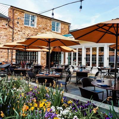 Outside seating area with tables set for guests, parasols, and planted flowers.