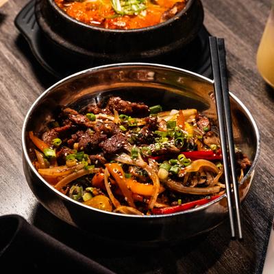 Beef bulgogi stir-fry loaded with onions, peppers and sesame seeds in a metal bowl.
