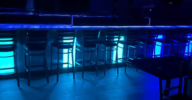 Interior, a bar counter with several bar stools, illuminated by blue neon or LED lighting