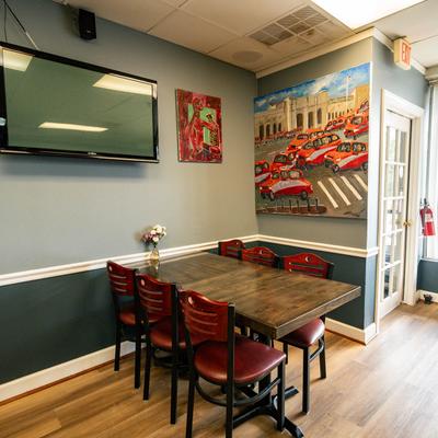 A corner with a  table and red chairs, wall adorned with a TV screen and vibrant artwork.
