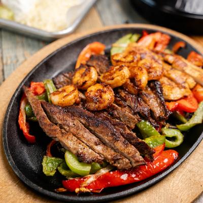 Mixed fajitas served on a hot cast-iron skillet with grilled bell peppers and onions.