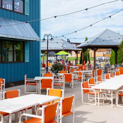 Outdoor restaurant patio with white tables and bright orange chairs, and gazebos.