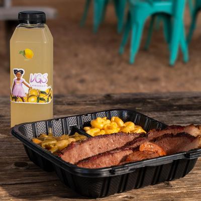 BBQ brisket with mac and cheese, greens, and a bottled lemonade on a wooden table.
