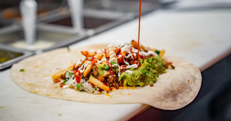 Bacon cheeseburger tortilla, with ground beef, rice, bacon, cheddar, guac, sour cream, and pico