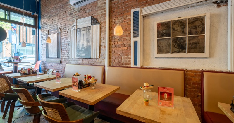 Interior with wooden tables, cushioned chairs, and exposed brick walls adorned with framed artwork and warm pendant lighting