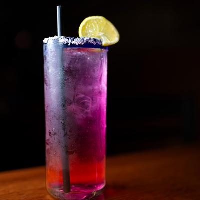 Red and purple cocktail drink, garnished with salt rim and a lemon slice.