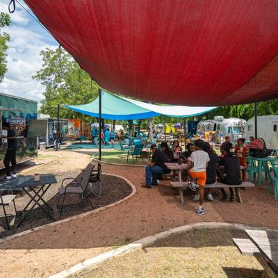 Parked food truck with outdoor seating with picnic tables under shades.