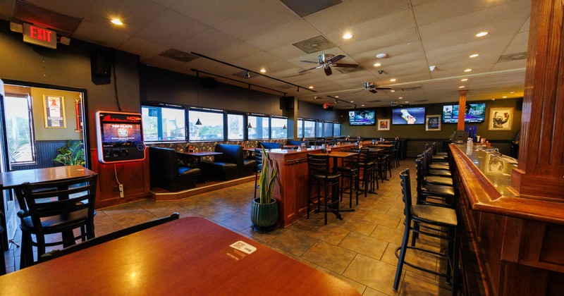 Interior of a casual restaurant with a bar, booths, and TVs