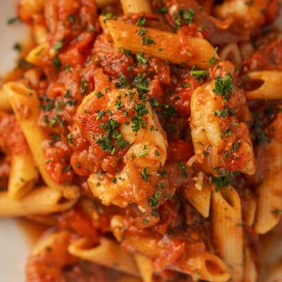 Penne pasta mixed with shrimp in a savory tomato sauce, close up.