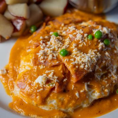 Fried eggs on tortillas with ham, sauce, cheese, and peas.